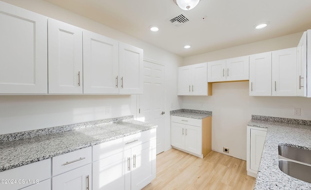 kitchen featuring light hardwood / wood-style floors, light stone countertops, white cabinetry, and sink