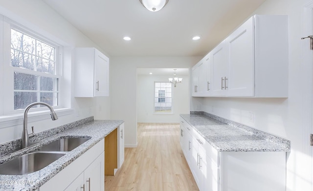 kitchen featuring an inviting chandelier, white cabinets, sink, light hardwood / wood-style floors, and light stone counters