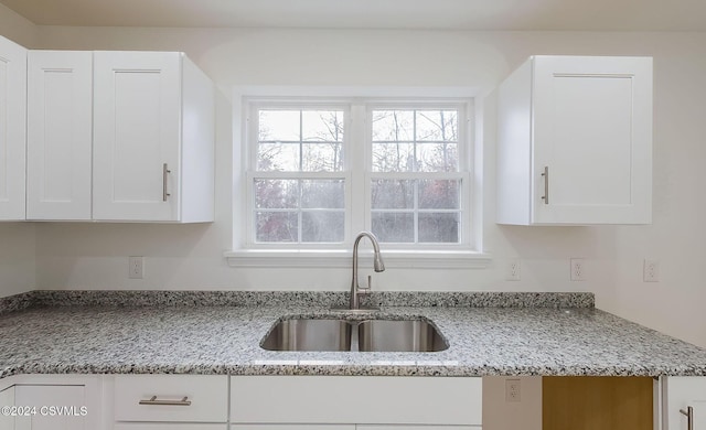 kitchen with light stone counters, white cabinetry, and sink