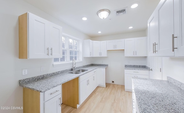 kitchen with light stone countertops, sink, white cabinets, and light hardwood / wood-style flooring