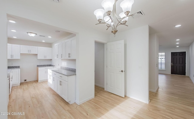 kitchen with stone counters, white cabinets, decorative light fixtures, light wood-type flooring, and a notable chandelier