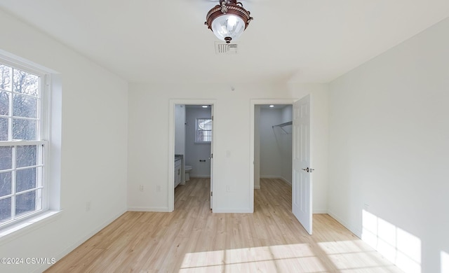 unfurnished bedroom featuring a closet, light wood-type flooring, a walk in closet, and multiple windows