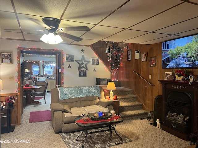 living room featuring carpet flooring, ceiling fan, a paneled ceiling, and wooden walls