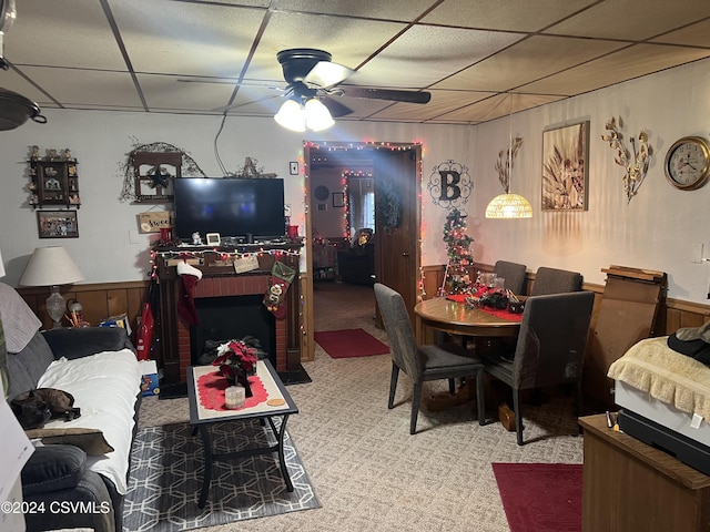 dining room with wood walls, ceiling fan, a drop ceiling, and light colored carpet