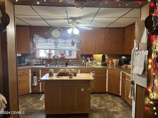 kitchen with a paneled ceiling, tasteful backsplash, ceiling fan, sink, and a kitchen island