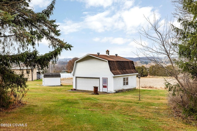 rear view of property with a mountain view, a yard, a garage, and a storage shed