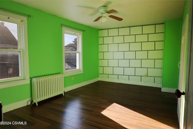 empty room featuring ceiling fan, dark hardwood / wood-style floors, and radiator heating unit