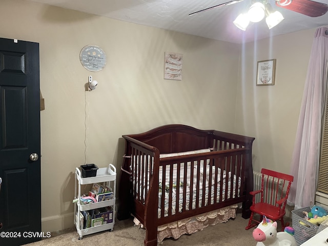 bedroom featuring light carpet, a nursery area, and ceiling fan