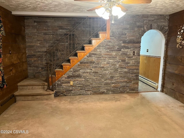 basement with wooden walls, ceiling fan, a baseboard radiator, and a textured ceiling