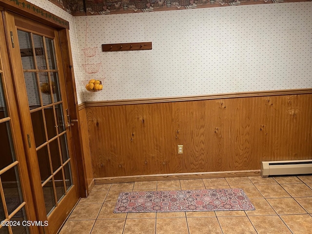 tiled empty room featuring baseboard heating and wooden walls