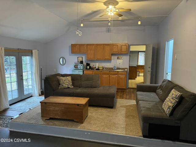 living room with ceiling fan, french doors, rail lighting, light hardwood / wood-style floors, and vaulted ceiling