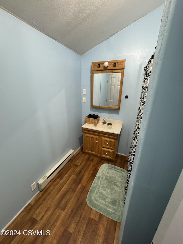 bathroom with vanity, lofted ceiling, a textured ceiling, baseboard heating, and wood-type flooring