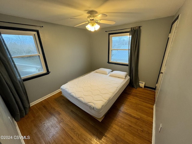 bedroom featuring ceiling fan, dark hardwood / wood-style floors, and a baseboard heating unit