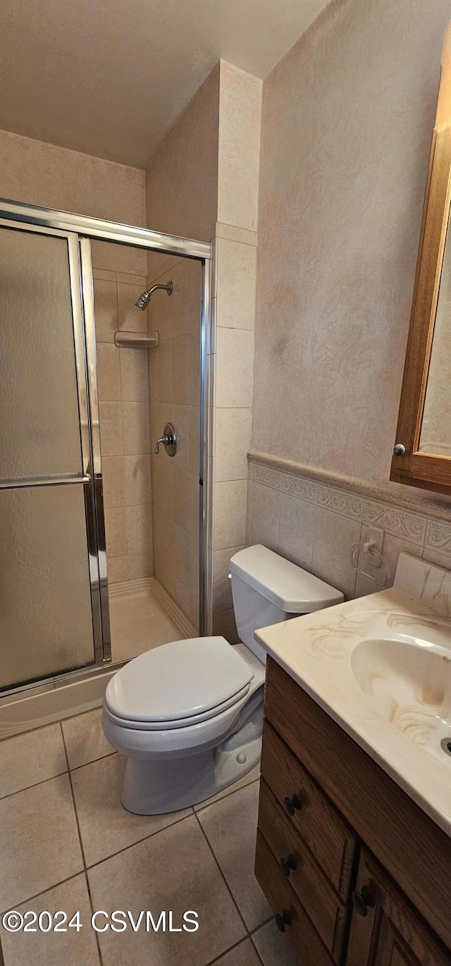 bathroom with vanity, a shower with door, tile walls, tile patterned flooring, and toilet