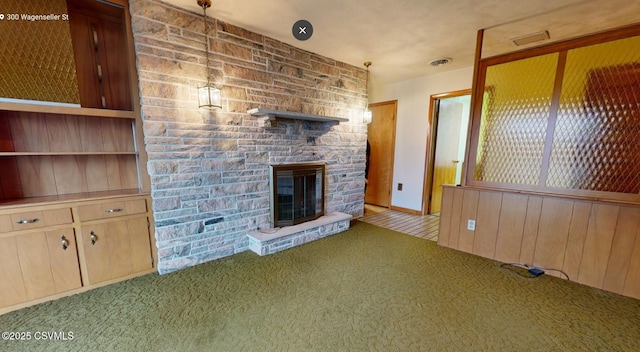 unfurnished living room with a stone fireplace, wooden walls, and light carpet