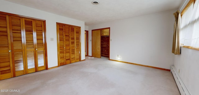 unfurnished bedroom featuring light carpet, baseboard heating, and multiple closets