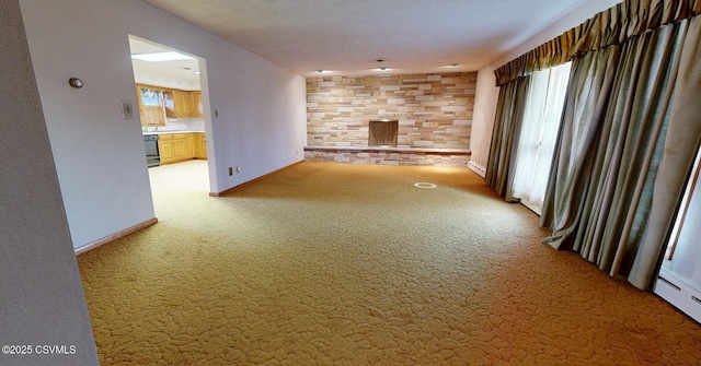 unfurnished living room featuring a healthy amount of sunlight, a stone fireplace, carpet floors, and a baseboard heating unit