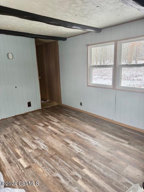 unfurnished bedroom featuring wood walls, beam ceiling, wood-type flooring, and a textured ceiling