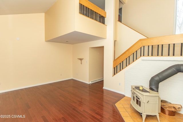 stairway featuring wood-type flooring, a towering ceiling, a wood stove, and a baseboard heating unit