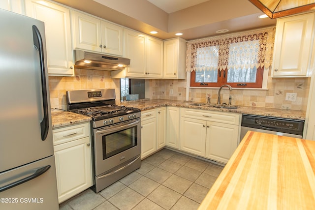 kitchen with light tile patterned floors, butcher block counters, stainless steel appliances, white cabinets, and sink