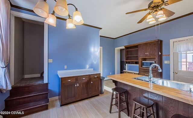 kitchen with hanging light fixtures, wood counters, a kitchen breakfast bar, light hardwood / wood-style flooring, and crown molding