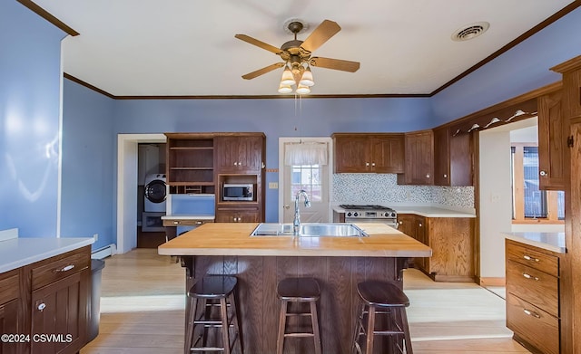 kitchen featuring sink, an island with sink, appliances with stainless steel finishes, washer / dryer, and butcher block counters