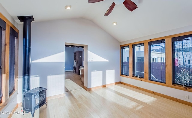 spare room with a wood stove, ceiling fan, light hardwood / wood-style flooring, and lofted ceiling