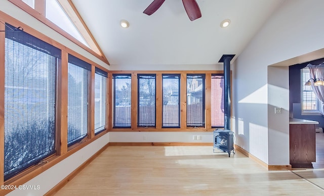 interior space with light hardwood / wood-style floors, a wood stove, ceiling fan, and lofted ceiling