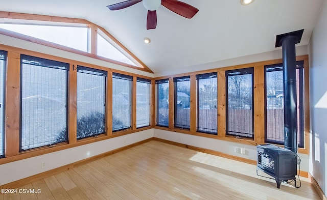 unfurnished room with a wood stove, ceiling fan, hardwood / wood-style floors, and vaulted ceiling