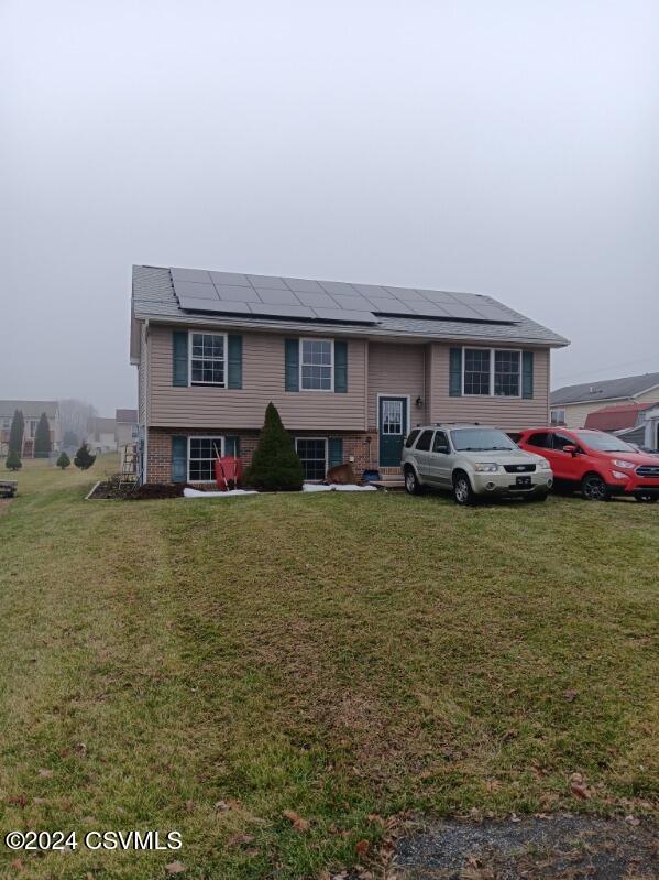 bi-level home featuring a front yard and solar panels