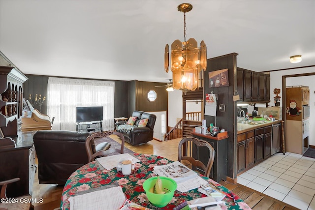 dining space with wood walls, sink, light tile patterned floors, and ceiling fan with notable chandelier