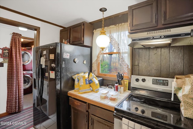 kitchen with pendant lighting, tile countertops, black fridge, electric range, and stacked washer / dryer