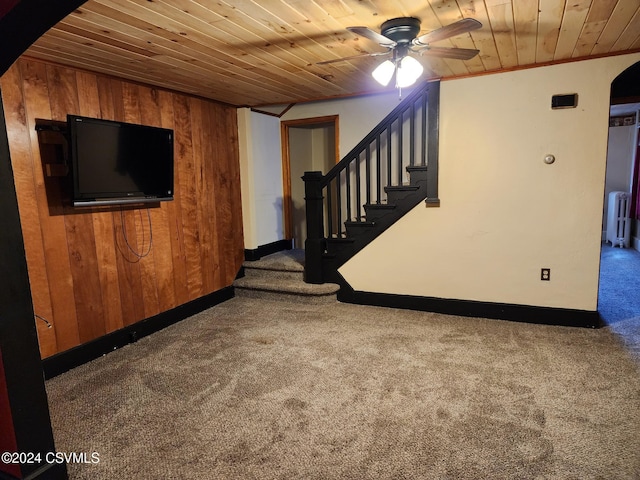 basement with dark colored carpet, ceiling fan, crown molding, and wood walls