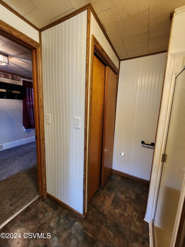 hallway featuring dark colored carpet, ornamental molding, and wooden walls