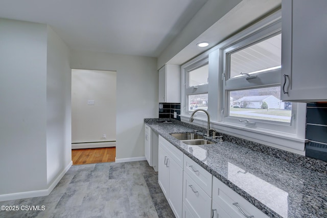 kitchen with white cabinetry, sink, baseboard heating, dark stone counters, and light wood-type flooring