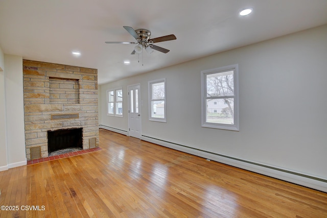 unfurnished living room with ceiling fan, a fireplace, light hardwood / wood-style floors, and a baseboard heating unit