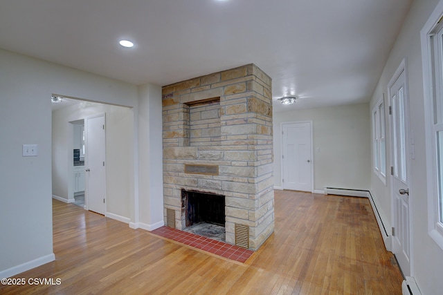 unfurnished living room with hardwood / wood-style floors, a stone fireplace, and a baseboard heating unit