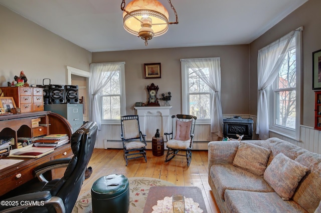 office area with light wood-type flooring, a wood stove, a wealth of natural light, and a baseboard heating unit