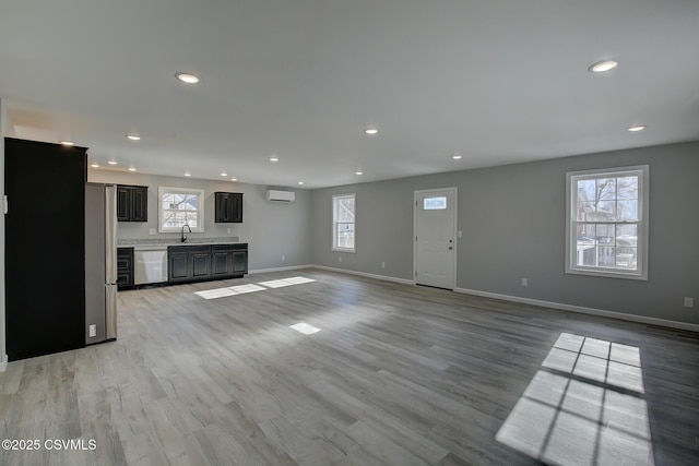 unfurnished living room featuring a wall mounted air conditioner and light hardwood / wood-style flooring