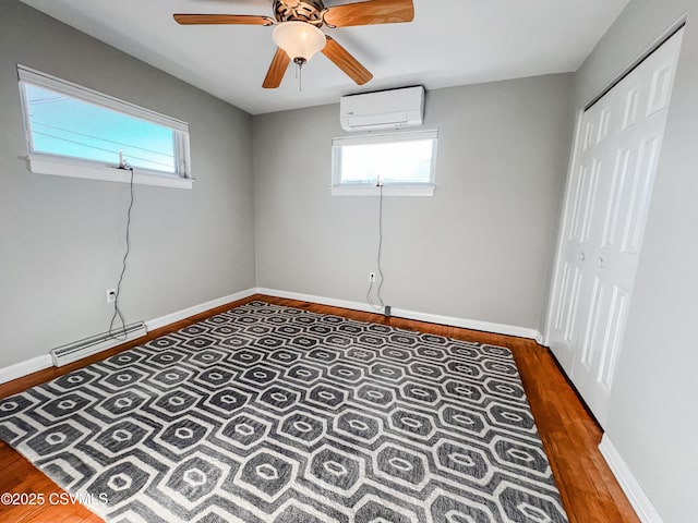 interior space with dark hardwood / wood-style floors, ceiling fan, baseboard heating, and a wall mounted AC