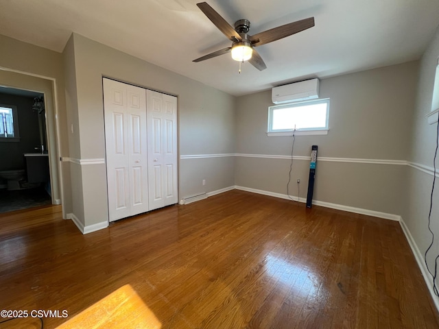 unfurnished bedroom with ceiling fan, a baseboard radiator, an AC wall unit, a closet, and hardwood / wood-style flooring