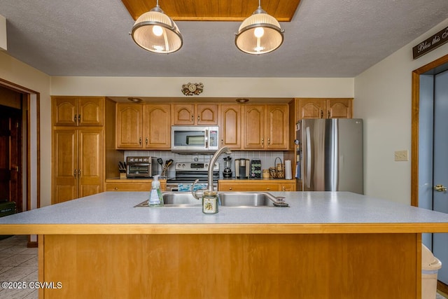 kitchen featuring an island with sink, appliances with stainless steel finishes, backsplash, pendant lighting, and sink