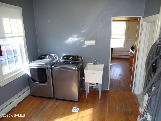 clothes washing area featuring baseboard heating, sink, washer and dryer, and hardwood / wood-style flooring