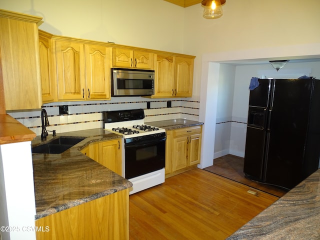 kitchen with decorative backsplash, black refrigerator with ice dispenser, sink, and range with gas cooktop