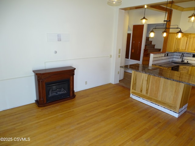 kitchen featuring pendant lighting, dark stone counters, sink, light wood-type flooring, and a kitchen bar