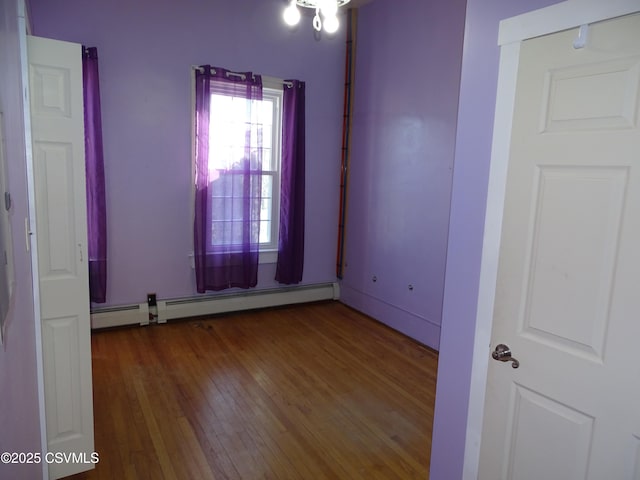 unfurnished room featuring baseboard heating and hardwood / wood-style floors