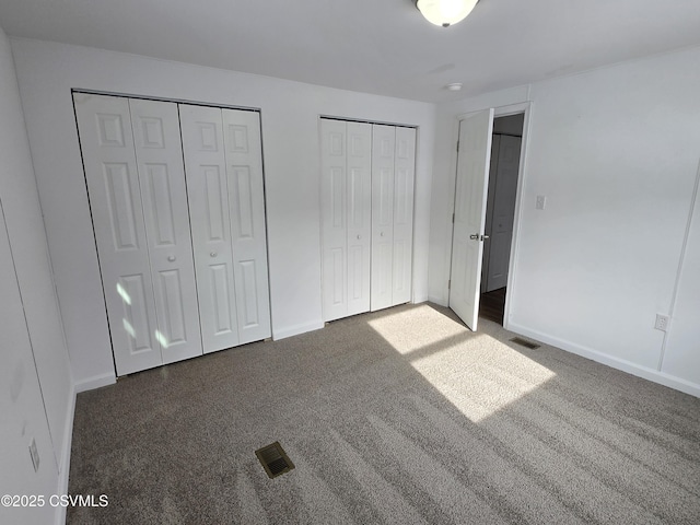 unfurnished bedroom featuring dark carpet and multiple closets