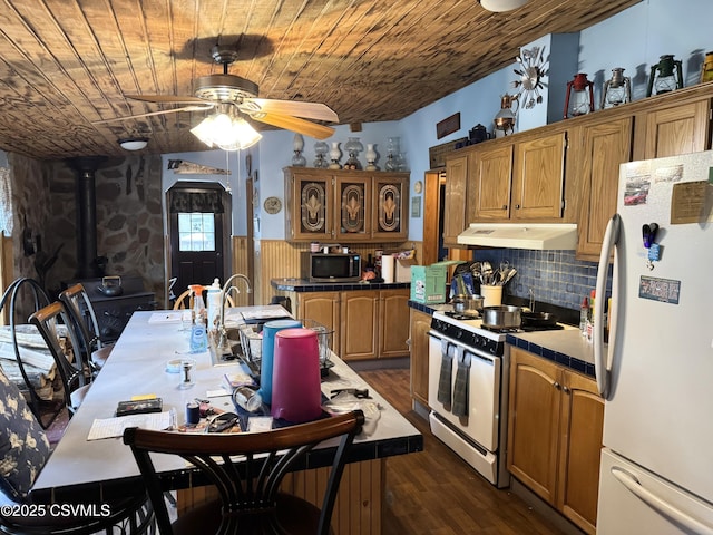 kitchen featuring a wood stove, wooden ceiling, dark hardwood / wood-style floors, white appliances, and a kitchen island with sink