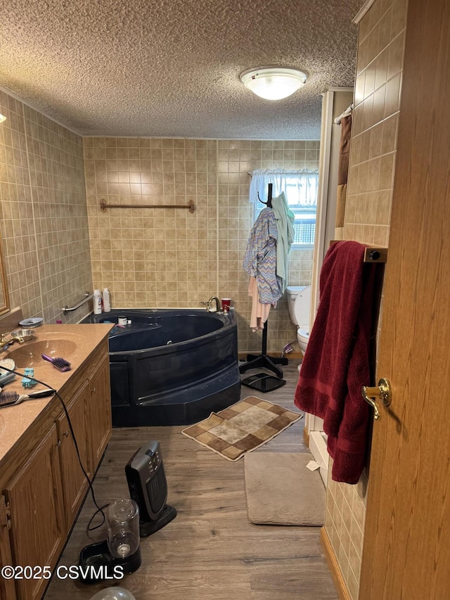 bathroom with tile walls, vanity, wood-type flooring, a textured ceiling, and a tub