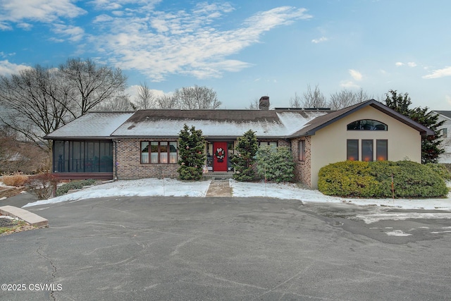 view of front of home featuring brick siding, a chimney, a sunroom, and stucco siding